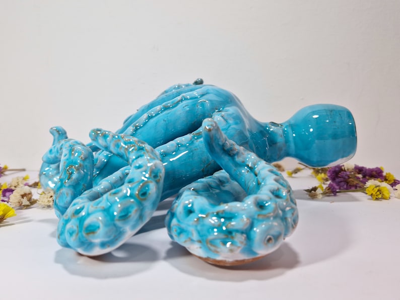 May include: A ceramic octopus sculpture with a blue and green glaze. The octopus has eight tentacles and is lying on its side.
