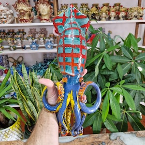 May include: A ceramic squid sculpture with a red, blue, and yellow color scheme. The squid has a checkered pattern on its body and tentacles.