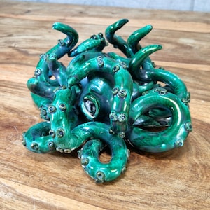 May include: A ceramic octopus sculpture with a green and blue glaze. The octopus has eight tentacles and is curled up in a ball.
