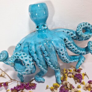 May include: A turquoise ceramic octopus sculpture with eight tentacles. The octopus has a textured surface and is glazed in a light blue color.