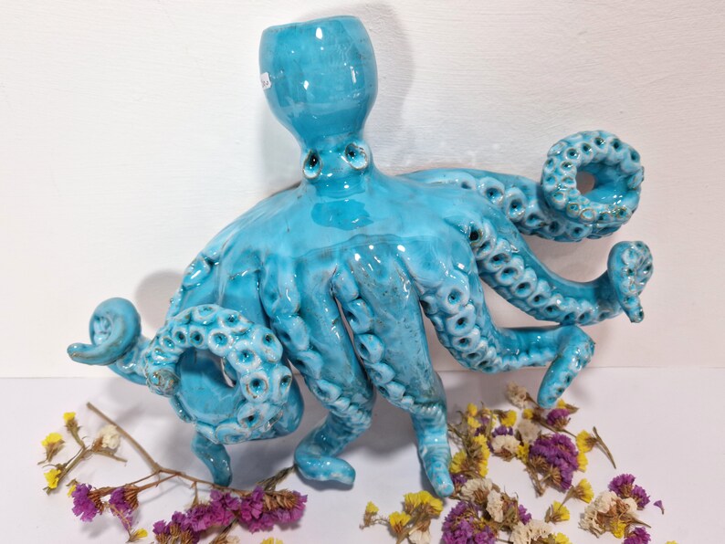 May include: A turquoise ceramic octopus sculpture with eight tentacles. The octopus has a textured surface and is glazed in a light blue color.