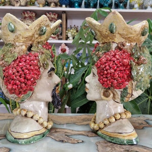 May include: Two ceramic planter heads with crowns, one male and one female, decorated with red berries and green leaves. The planters are hand-painted and have a rustic, vintage style.