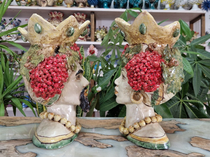 May include: Two ceramic planter heads with crowns, one male and one female, decorated with red berries and green leaves. The planters are hand-painted and have a rustic, vintage style.