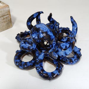 May include: A ceramic octopus sculpture with a glossy blue and black glaze. The tentacles are curled, and the sculpture has a detailed, textured surface. The octopus is a decorative item.
