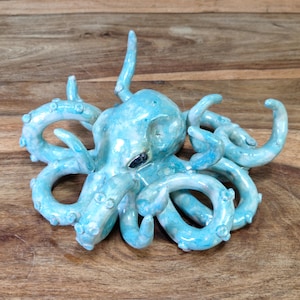 May include: A ceramic octopus sculpture with a light blue and white glaze. The octopus has eight tentacles and is curled up in a relaxed pose.