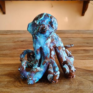 May include: A ceramic octopus sculpture with a textured surface. The octopus is primarily blue with brown and white accents. The sculpture is displayed on a wooden surface.