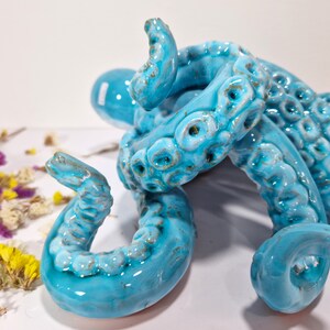 May include: A blue ceramic octopus sculpture with detailed tentacles. The octopus is curled up in a compact shape, with its tentacles intertwined.