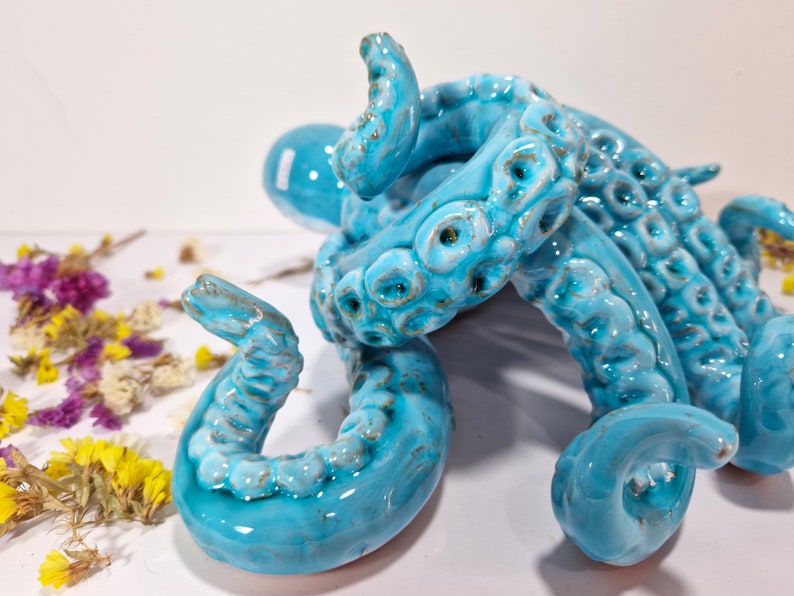 May include: A blue ceramic octopus sculpture with detailed tentacles. The octopus is curled up in a compact shape, with its tentacles intertwined.