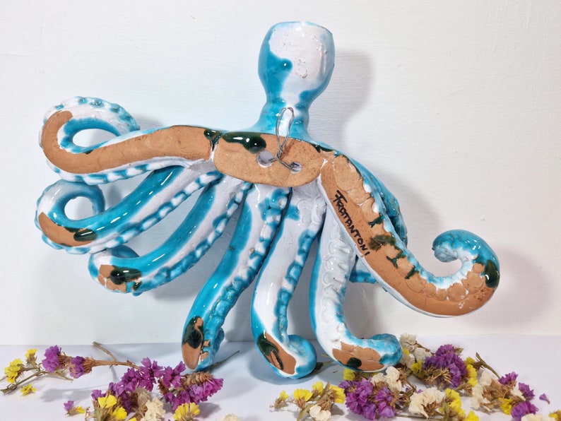 May include: A blue and white ceramic octopus wall hanging with a brown base. The octopus has eight tentacles and is signed "Frammutoni".