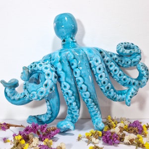 May include: A ceramic octopus sculpture with a blue glaze and detailed tentacles. The octopus is positioned with its tentacles curled and reaching out.