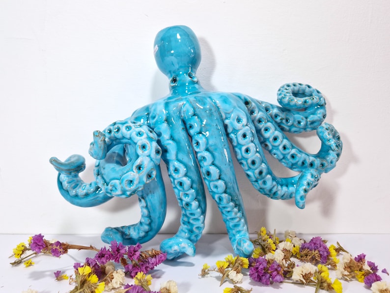 May include: A ceramic octopus sculpture with a blue glaze and detailed tentacles. The octopus is positioned with its tentacles curled and reaching out.