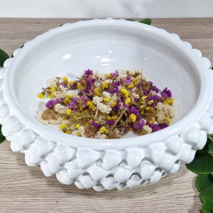 May include: White ceramic bowl with a textured, raised rim. The bowl is filled with dried flowers in shades of purple, yellow, and white.