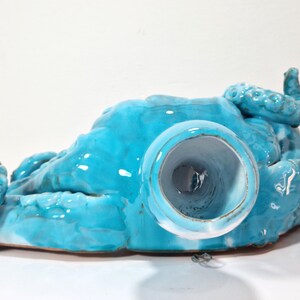 May include: A turquoise ceramic octopus sculpture with a hollow center. The octopus is lying on its back with its tentacles spread out.