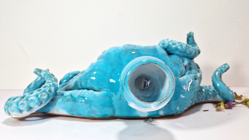 May include: A turquoise ceramic octopus sculpture with a hollow center. The octopus is lying on its back with its tentacles spread out.