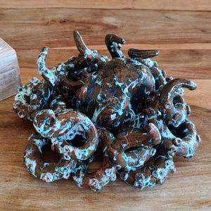 May include: A ceramic octopus sculpture with a brown and blue marbled finish. The sculpture features multiple tentacles and a detailed, textured surface. The octopus is a decorative item, suitable for home decor.