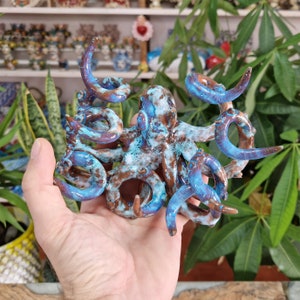 May include: A ceramic octopus figurine with blue and brown glaze. The octopus has eight tentacles that are curled and twisted. The figurine is hand-painted and has a unique, rustic look.
