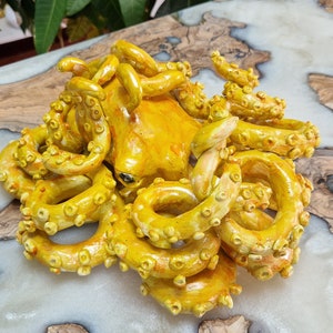 May include: A yellow ceramic octopus sculpture with detailed tentacles. The octopus is curled up with its tentacles intertwined.