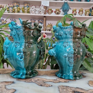 May include: Two ceramic vases with a blue and green glaze. The vases are decorated with faces and have a whimsical, cartoonish style.