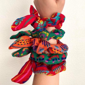 May include: A set of four colorful hair scrunchies with a traditional Mexican design. The scrunchies are made of woven fabric and feature a variety of colors, including red, green, orange, and blue.