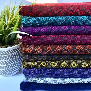 May include: A stack of eight colorful woven fabric strips with a geometric diamond pattern. The fabric is folded and stacked in a rainbow pattern, starting with red and ending with dark blue.