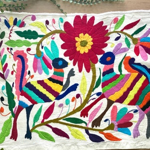 May include: A colorful embroidered wall hanging featuring two stylized animals with striped bodies and floral designs. The animals are surrounded by a variety of flowers and leaves in shades of pink, red, yellow, green, and blue.