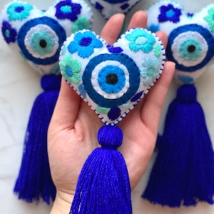 May include: Four blue and white embroidered felt heart-shaped ornaments with a blue evil eye design and blue tassels.
