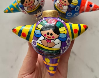 May include: Three colorful star-shaped ornaments with a traditional Mexican folk art design. Each ornament features a smiling woman wearing a colorful dress and a flower crown. The ornaments are painted in vibrant colors, including red, orange, yellow, green, blue, and purple.