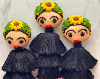 May include: Three black tassel keychains with embroidered felt faces. Each face has a yellow sunflower with green leaves, black eyelashes, and red lips.
