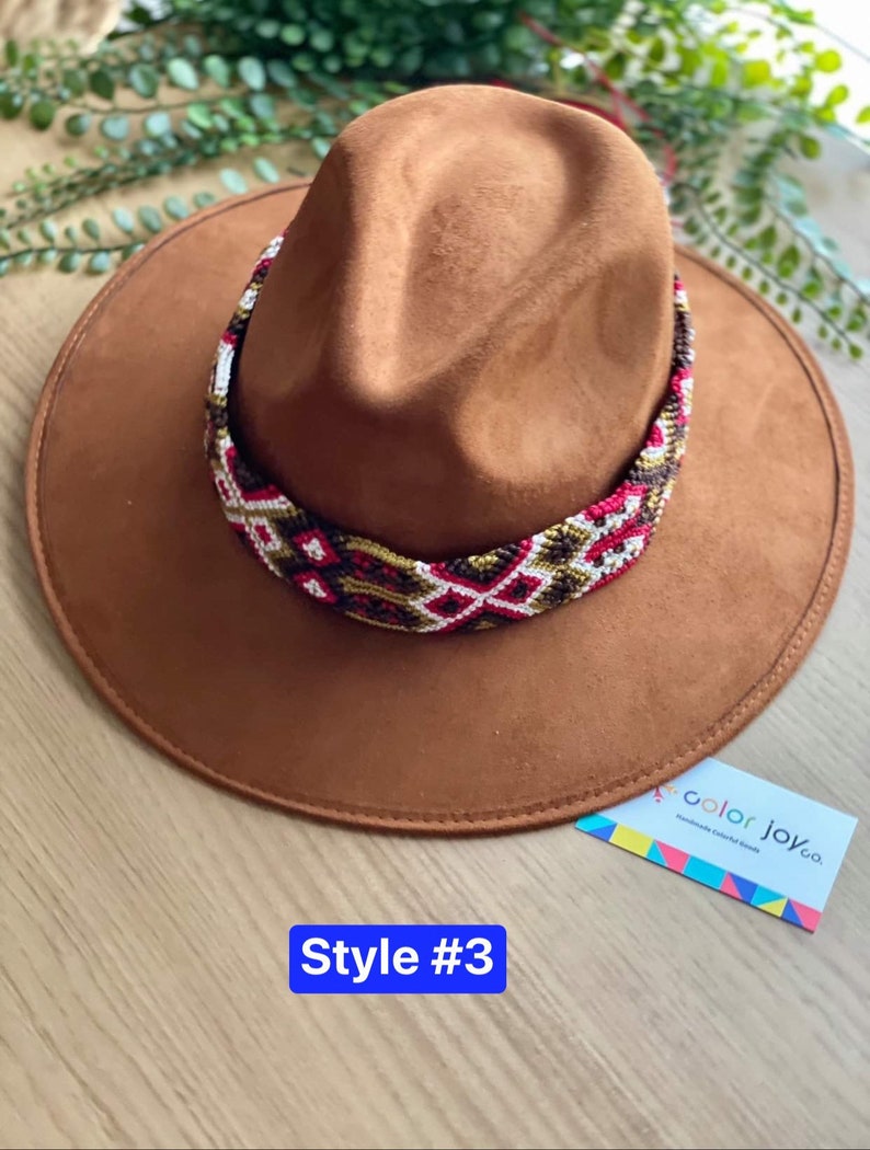 May include: A brown suede fedora hat with a colourful woven band. The band features geometric patterns in red, white, gold, and black. The hat is labelled "Style #3" and "color joy co."