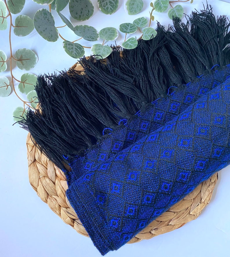 May include: A black and blue woven shawl with a geometric pattern and black fringe.