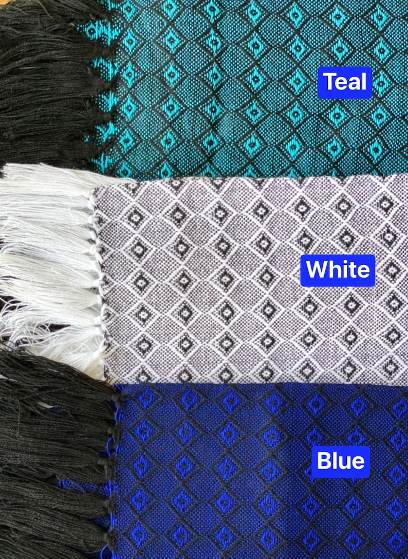 May include: Three fabric scarves with fringe edges. The top scarf is teal with a black and white diamond pattern. The middle scarf is white with a black diamond pattern. The bottom scarf is blue with a black diamond pattern. The text "Teal", "White", and "Blue" is printed on each scarf.