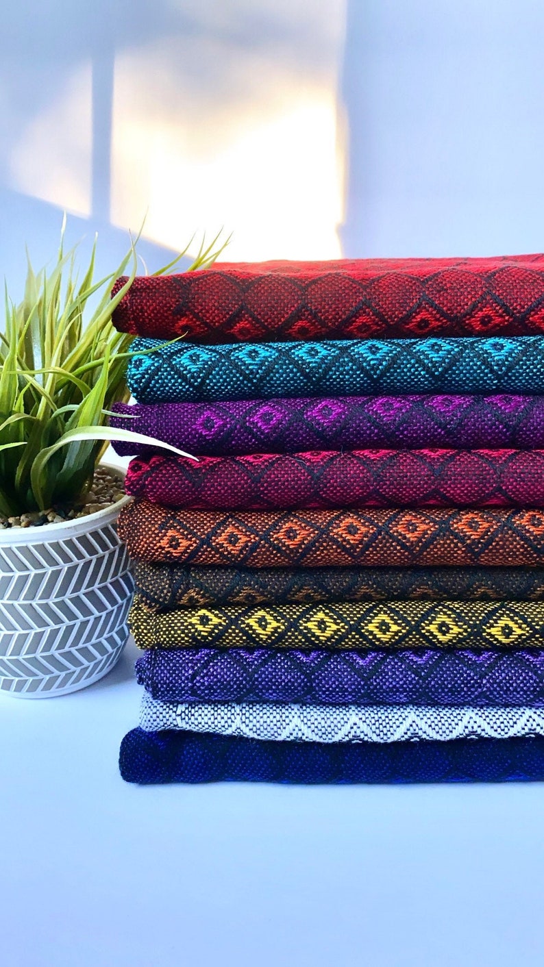 May include: A stack of eight colorful woven fabric strips with a geometric diamond pattern. The fabric is folded and stacked in a rainbow pattern, starting with red and ending with dark blue.