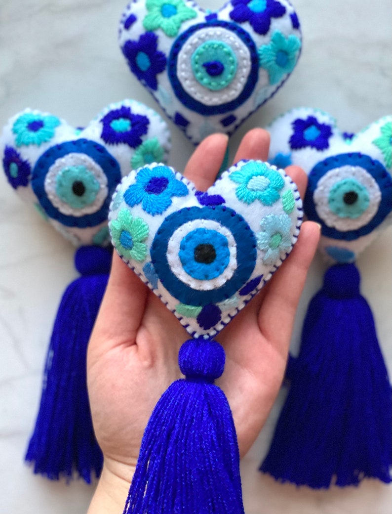 May include: Four blue and white embroidered felt heart-shaped ornaments with a blue evil eye design and blue tassels.