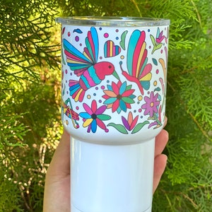 May include: White tumbler with a colorful hummingbird and butterfly design. The design features flowers, hearts, and geometric patterns in shades of pink, blue, green, yellow, and orange.