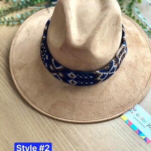 May include: A brown suede cowboy hat with a blue and white beaded band. The hat is sitting on a wooden surface. The text "Style #2" is visible in the lower left corner of the image.