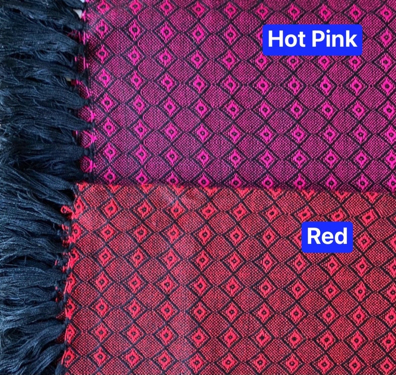 May include: A close-up of a fabric with a black and red diamond pattern. The top half of the fabric is hot pink and the bottom half is red. The fabric has black fringe on the left side.