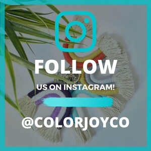 May include: A colorful rainbow macrame wall hanging with tassels. The macrame is made with natural fibers and has a variety of colors, including red, orange, yellow, green, blue, and purple. The wall hanging is hanging from a metal ring. The image also includes the text "FOLLOW US ON INSTAGRAM! @COLORJOYCO".