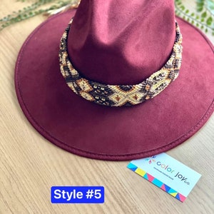 May include: A burgundy felt fedora hat with a brown and white beaded band. The hat has a wide brim and a tall crown. The band is made of small beads that are woven together in a geometric pattern. The hat is labelled "Style #5" and "color joy co. Handmade Colorful Goods".