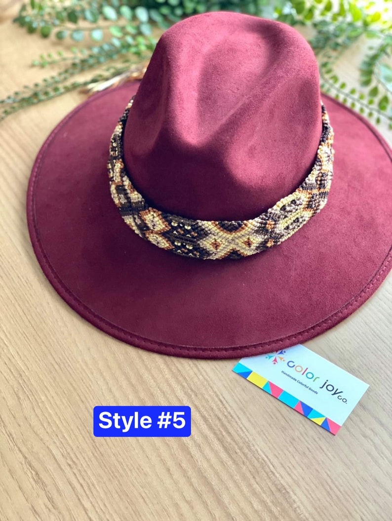 May include: A burgundy felt fedora hat with a brown and white beaded band. The hat has a wide brim and a tall crown. The band is made of small beads that are woven together in a geometric pattern. The hat is labelled "Style #5" and "color joy co. Handmade Colorful Goods".