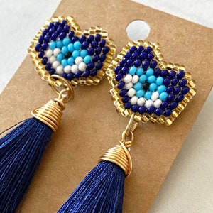 May include: A pair of blue and gold earrings with a beaded evil eye charm and a blue tassel.