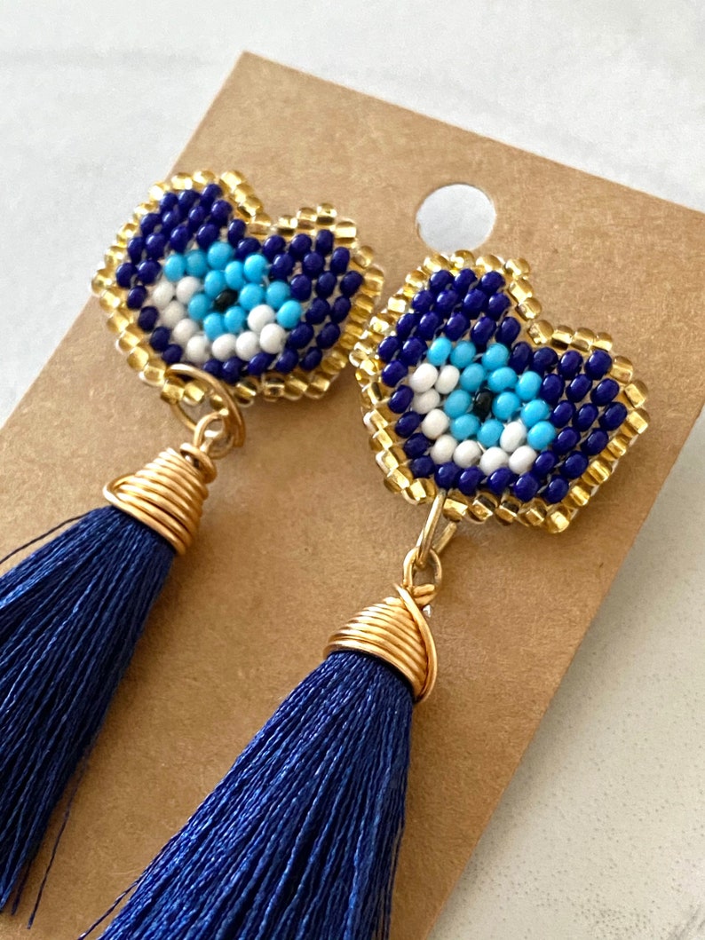 May include: A pair of blue and gold earrings with a beaded evil eye charm and a blue tassel.