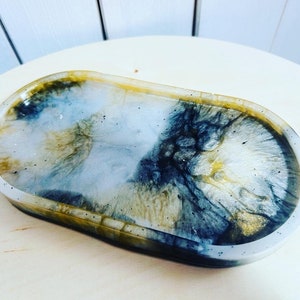 May include: An oval-shaped resin tray with a white, black, and gold marbled design. The tray is ideal for holding jewellery, keys, or other small items.