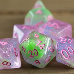 May include: A set of six iridescent dice with pink and green swirls and glitter. The dice are numbered 1-20 and have pink numbers.