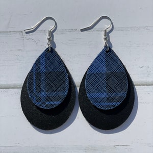 May include: A pair of layered teardrop earrings. The top layer features a blue and black plaid pattern, while the bottom layer is solid black. The earrings have silver-colored fish hook ear wires.