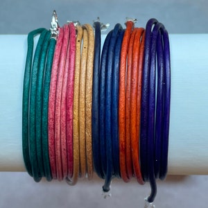 May include: A set of ten leather bracelets in various colors, including green, pink, gold, navy blue, orange, and purple. The bracelets are stacked together and have silver clasps.