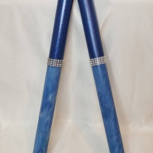 May include: Two cylindrical drumsticks featuring a deep navy blue upper section with a subtle shimmer and a lighter blue marbled lower section. Each stick is accented with a band of silver-toned rhinestones separating the two distinct blue colors.