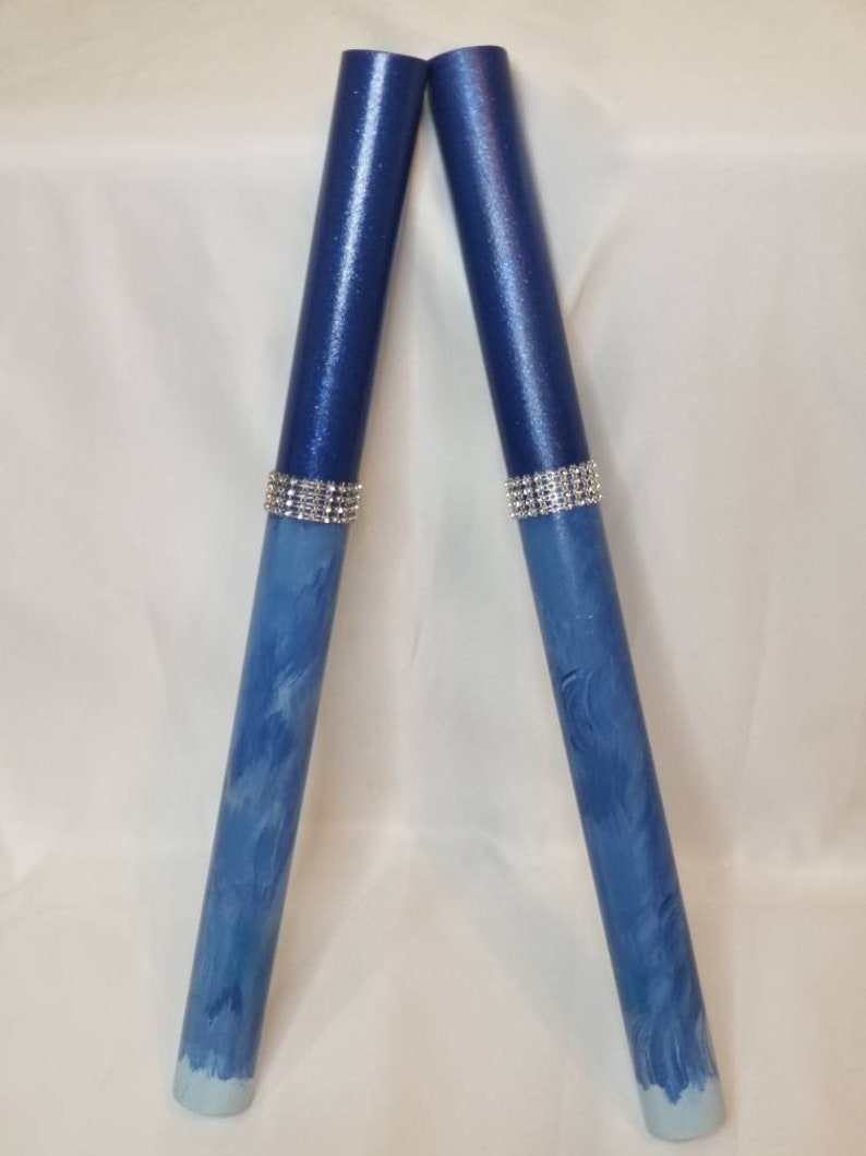 May include: Two cylindrical drumsticks featuring a deep navy blue upper section with a subtle shimmer and a lighter blue marbled lower section. Each stick is accented with a band of silver-toned rhinestones separating the two distinct blue colors.