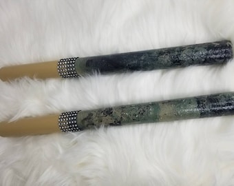 May include: Two cylindrical wands featuring a smooth tan handle separated by a band of small, clear, reflective rhinestones from a textured, mottled dark green and black shaft that has a glossy, uneven finish across the surface of the tubes.
