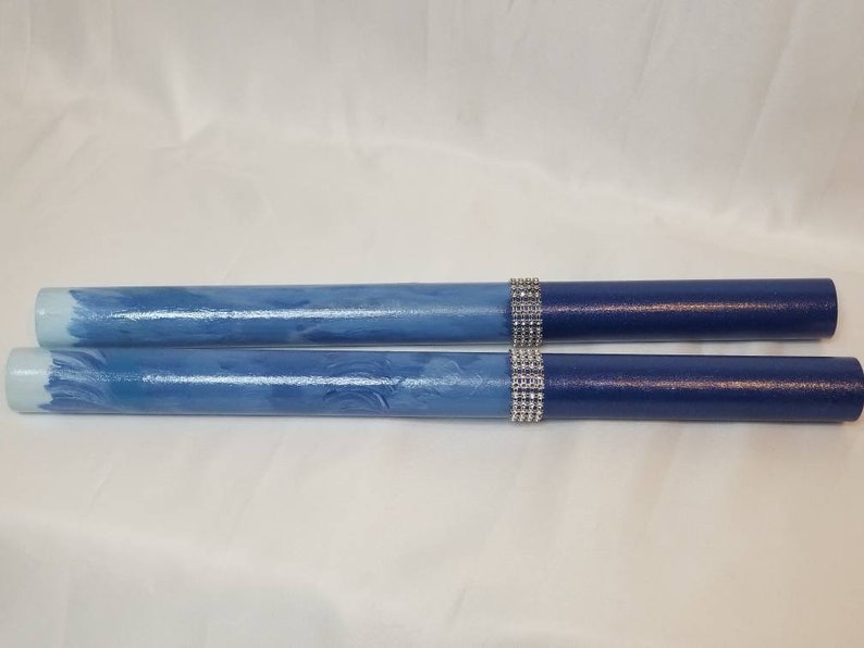 May include: Two cylindrical sticks featuring a gradient finish that transitions from a light blue at the ends to a deep navy blue. Each stick is accented with a band of silver-toned rhinestones positioned between the two blue color sections.