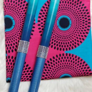 May include: Two cylindrical taper candles featuring a blue ombre gradient from light to dark. Each candle is accented with a band of silver-toned rhinestones around the center. The candles are placed over a square fabric with a pink and blue circular pattern.